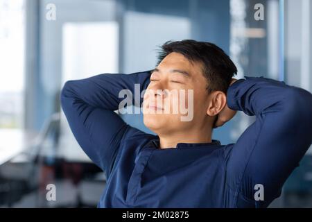 Asiatischer Geschäftsmann, der im Büro ruht, Mann im Hemd, Nahaufnahme mit Händen hinter dem Kopf, Träume und visualisiert gewünschte Pläne und Leistungen. Stockfoto