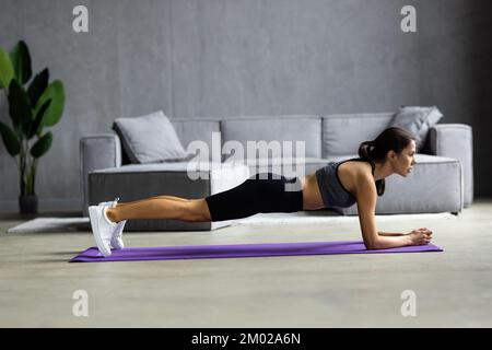 Fit junge Frau trägt Sportkleidung zu Hause zu arbeiten tun Planken Übung auf Teppich Stockfoto