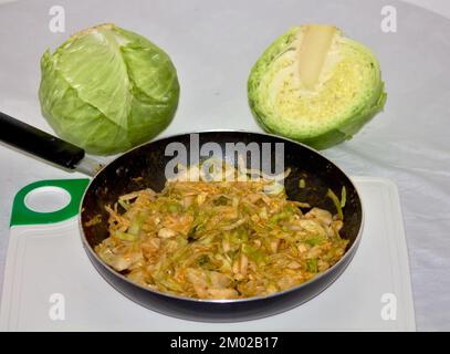 Kohl mit Tomatensauce in einem Topf gekocht, auf der Rückseite zwei Kohlköpfe, ein ganzer und ein weiterer in zwei Hälften gehackt Stockfoto