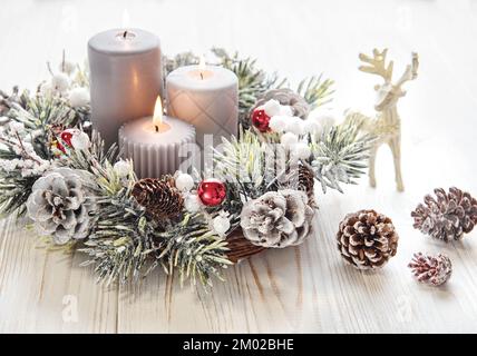 Dekorierter Adventskranz aus Tannenzweigen mit brennenden Kerzen, Tradition in der Zeit vor Weihnachten. Weißer, alter Holzhintergrund. Stockfoto