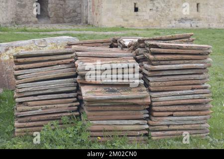 Alte Tonfliesen sind auf grünem Gras gestapelt, vor dem Hintergrund einer alten Steinwand. Speicherplatz kopieren. Selektiver Fokus. Stockfoto
