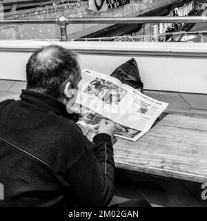 Ein Mann liest eine Zeitung, während er eine Schüssel Suppe im Cardiff Indoor Market isst. Klare Aufnahme des Artikels über PM Sunak. Schwarzweißfoto Stockfoto