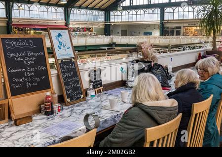 Vier Frauen unterhalten sich in einem Café auf der obersten Ebene des Victorian Indoor Market in Cardiff. Glasdach und Marmorablageflächen. Menü. Stockfoto