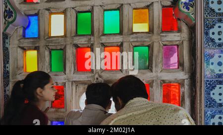 Stadtpalast mit farbenfrohem Fensterblick in Udaipur, Rajasthan, Indien. Die Leute schauen auf die Stadt, draußen von Mosaikfenstern im Museum. Innen, Innenansicht Stockfoto