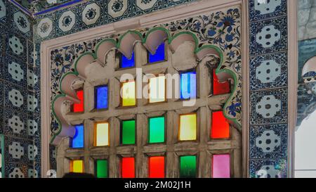 Stadtpalast mit farbenfrohem Fensterblick in Udaipur, Rajasthan, Indien. Die Leute schauen auf die Stadt, draußen von Mosaikfenstern im Museum. Innen, Innenansicht Stockfoto