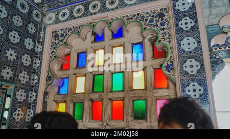 Stadtpalast mit farbenfrohem Fensterblick in Udaipur, Rajasthan, Indien. Die Leute schauen auf die Stadt, draußen von Mosaikfenstern im Museum. Innen, Innenansicht Stockfoto