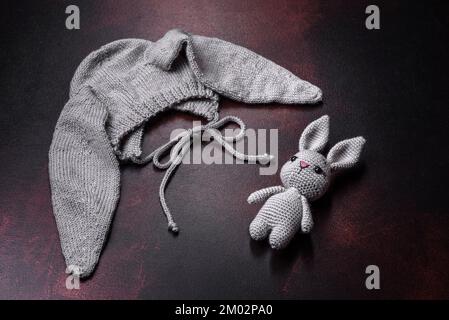 Niedlicher grauer Strickmütze mit Ohren für ein kleines Baby mit einer Strickpuppe in Form eines Hasen Stockfoto