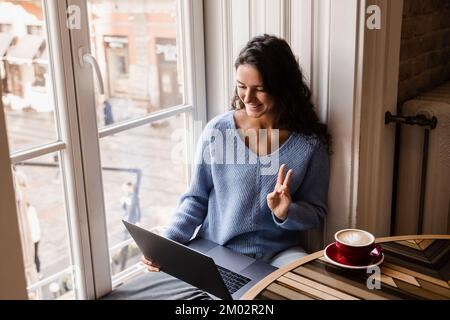 Eine Bloggerin mit Laptop chattet online über eine Videoverbindung mit ihren Abonnenten. Glückliche junge Geschäftsfrau unterhält sich mit Kollegen und hat es getan Stockfoto