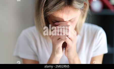 Eine gestresste, traurige Frau mit geschlossenen Augen hält ihre Hände nahe ihrem Gesicht nah dran. Stockfoto