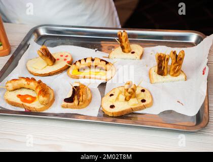 Hot Dog mit verschiedenen Gewürzen und Chili, Paprika und Tomaten und Soßen, Senf und Ketchup auf einem eisernen Tablett auf einem weißen Tisch. Stockfoto