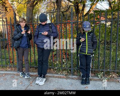 Jungs klebten an ihren Handys und warteten darauf, dass ein Stadtbus nach der Schule in Brooklyn, New York, nach Hause fährt. Stockfoto