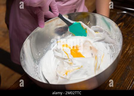Rühren Sie das Eigelb mit einem Acrylspatel in einer Metallschüssel in das gepeitschte Weiß Stockfoto
