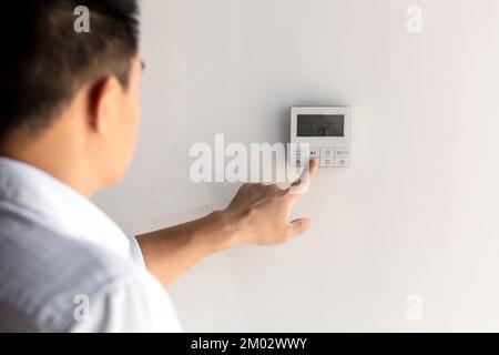 Nahaufnahme. Der Finger eines Mannes Hand in einem weißen Hemd beinhaltet die Knöpfe des Bedienfelds der Klimaanlage an der Wand des Hauses, Büro. Stockfoto