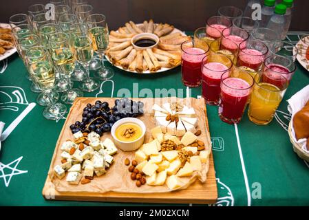 Snacktisch. Gläser Champagner, Gläser Saft und Leckereien. Käseplatte mit verschiedenen Käsesorten, Nüssen und Trauben. Platte mit Federrolle Stockfoto