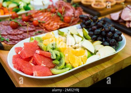 Ein Teller mit geschnittenem Obst auf dem Snacktisch. Scheiben Kiwi, Grapefruit, Birne und Trauben. Stockfoto