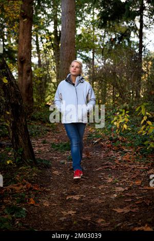 Eine attraktive blonde Frau, die im Wald auf einer Wanderung durch die Natur spaziert Stockfoto