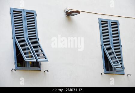 Zwei Fenster mit blauen Fensterläden und eine elektrische Laterne an der Fassade eines Gebäudes in einer Passera in Florenz, Italien Stockfoto