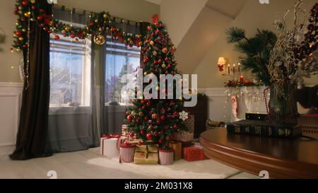 Baum mit Bällen, Spielzeug, blinkenden Lichtern, Geschenkverpackungen und Geschenkkisten stehen im Wohnzimmer. Weihnachten und Neujahr festliche Innendekoration. Atmosphäre in gemütlichem Apartment an Winterferien. Stockfoto