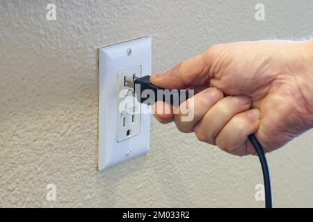 Die Hand eines Mannes, der das Netzkabel an die Stromversorgung anschließt Stockfoto