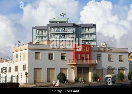 Leute, die am IRGA-Gebäude in Asmara vorbeigehen, im frühen Morgenlicht Stockfoto