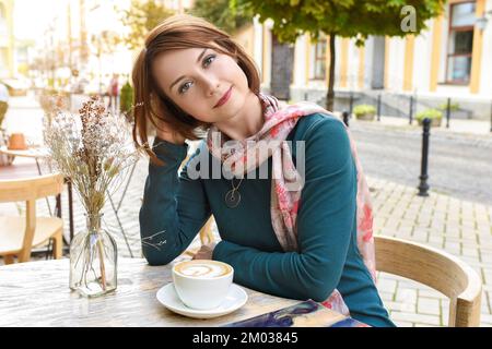 Außenporträt eines jungen Mädchens, das morgens eine Tasse Kaffee in einem Restaurant trinkt Stockfoto