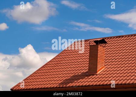 Teil des Hauses mit einem braunen Fliesendach und einem Kamin am Himmel. Metalldach Stockfoto