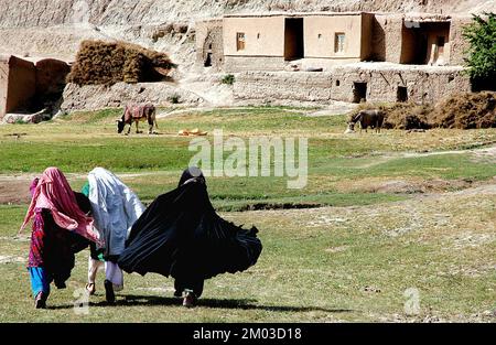 Ein kleines Dorf zwischen Chaghcharan und dem Minarett von Jam, Provinz Ghor in Afghanistan: Drei junge Frauen in traditioneller Kleidung laufen über ein Feld. Stockfoto