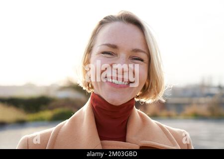 Glückliche Erwachsene Lady bei Sonnenuntergang, die aufblickt und sich in die Kamera dreht und die Natur mit frischer Luft genießt Stockfoto