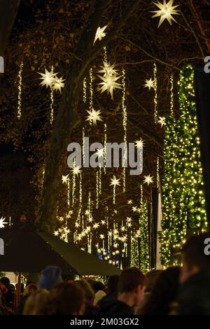 Nachtatmosphäre des Weihnachtsmarkts, Weihnachtsmarkt in Köln, mit dekorierten beleuchteten Verkaufsständen und hängenden Sternenlampen am neumarktplatz. Stockfoto