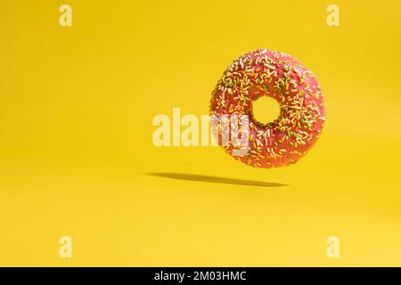 Schwebender rosa Donut auf gelbem Hintergrund. Kreativer kulinarischer Hintergrund Stockfoto