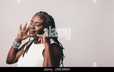 Reife Frau mit Dreadlocks, die ihre Lieblingsmusik über bluetooth-Ohrstöpsel genießt. Eine Frau mittleren Alters, die eine Playlist hört, während sie gegen einen Stu steht Stockfoto