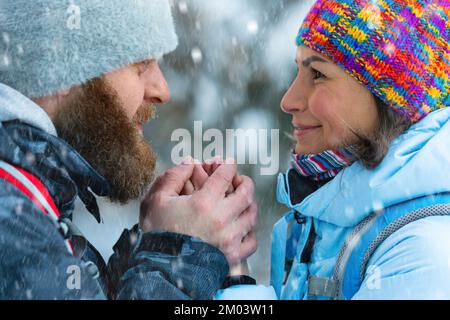 Ein paar Wanderer mittleren Alters im Winterwald. Der Mann wärmt die Hände der Frau mit seinem Atem. Nahaufnahme. Stockfoto