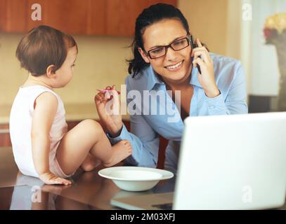 Alle Mütter sind berufstätige Mütter. Eine beschäftigte junge Mutter zu Hause mit ihrem Baby. Stockfoto