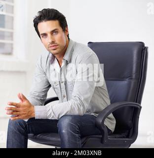 Er hat einen schwelenden Blick... ein gutaussehender junger Mann, der auf einem Stuhl sitzt. Stockfoto