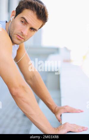 Das Aufwärmen gehört zu seinem Fitness-Ritual. Abgeschnittenes Bild eines attraktiven jungen Mannes, der sich an eine Wand lehnt. Stockfoto