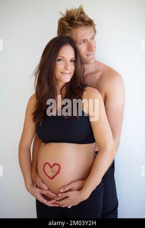 Eine Bindung zu teilen, die nie verblassen wird. Ein junges, erwartendes Paar, das zusammensteht, mit einer Herzform auf dem erwarteten motheramp039s-Bauch. Stockfoto