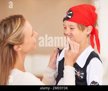 Jeder Pirat braucht einen Schnurrbart - eine letzte Geste der Mutter. Ein lächelnder Junge, der vor seiner Mutter steht und einen Schnurrbart auf sein Gesicht malt. Stockfoto