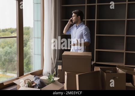 Vielbeschäftigter Mann, der mit einem Smartphone über einen Haufen Papierkartons spricht Stockfoto