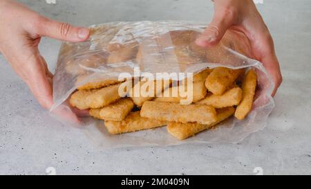 Panierte Fischstäbchen gefroren. Plastiktüte mit Fischstäbchen in knuspriger goldener Panade auf dem Küchentisch Stockfoto