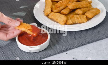 Fischstäbchen in einer knusprigen goldenen Panade und eine Schüssel Ketchup aus nächster Nähe auf dem Küchentisch Stockfoto