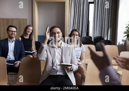 Lächelnder Teilnehmer des Business Trainings hebt die Hand und stellt dem Sprecher eine Frage Stockfoto