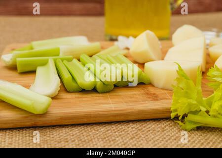 Nahaufnahme von grünen Selleriestangen, rohen Kartoffeln und Zwiebeln auf dem Küchentisch. Selleriesuppen-Rezept, Zutaten aus der Nähe Stockfoto