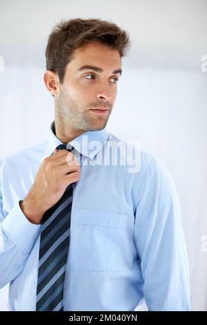 Sie sehen umwerfend aus wie immer. Ein gutaussehender Geschäftsmann, der über seine Schulter guckt, während er seine Krawatte justiert. Stockfoto