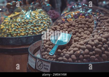 Eine Vielzahl von runden Schokoladenbonbons in einem Kunststoffspender mit einem Löffel oder einer Schaufel zum Herausnehmen. Süßigkeitenladen-Szene. Stockfoto