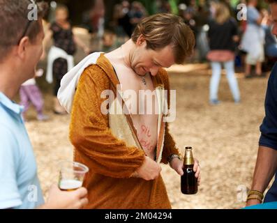 Für den lustigen Anlass. Ein junger Mann, der seinen Affenanzug aufmacht, während er ein Bier auf einem Festival hält. Stockfoto