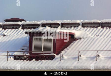 Große Eiszapfen auf dem Dach des Hauses an einem verschneiten Wintertag. Dachreinigung von Schnee und Eiszapfen. Stockfoto