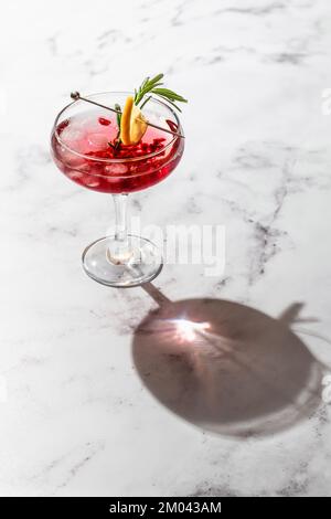 Granatapfelsaft-Eiscocktail mit Rosmarin und Zitrone auf weißem Marmorhintergrund isoliert mit klaren Schatten in hartem Licht, Platz für Text. Weihnachten Stockfoto