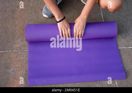 Frauenhände Rollen draußen die Matte hoch. Sportlerin, die nach dem Training die Matte hochrollt. Konzept der Aufrollmatte nach Übung, Managua, Ni Stockfoto