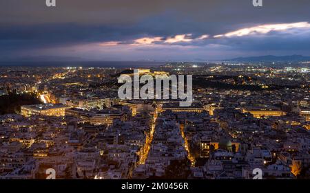 Blick über das Meer der Häuser von Athen, beleuchteter Parthenon-Tempel auf der Akropolis, dramatisch bewölkter Himmel bei Sonnenuntergang, vom Berg Lycabettus, Athen, Gr Stockfoto