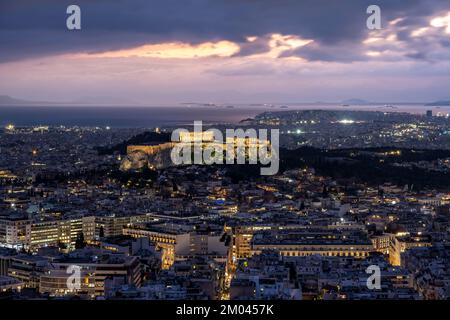 Blick über das Meer der Häuser von Athen, beleuchteter Parthenon-Tempel auf der Akropolis, dramatisch bewölkter Himmel bei Sonnenuntergang, vom Berg Lycabettus, Athen, Gr Stockfoto